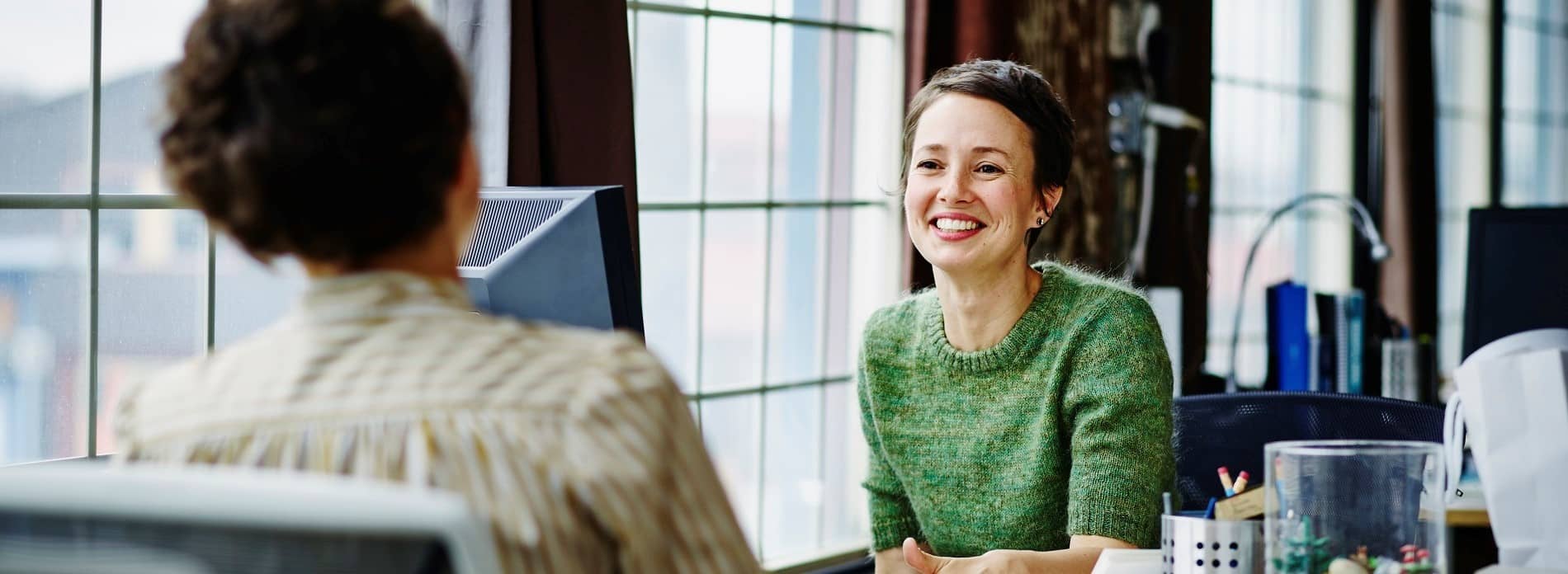 Two women at work chatting over desk
